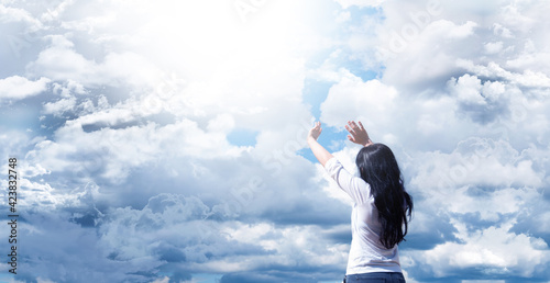 Young girl with raised arms. Against a background of blue sky and clouds. Joy. Prayer and worship to God. © amdre100