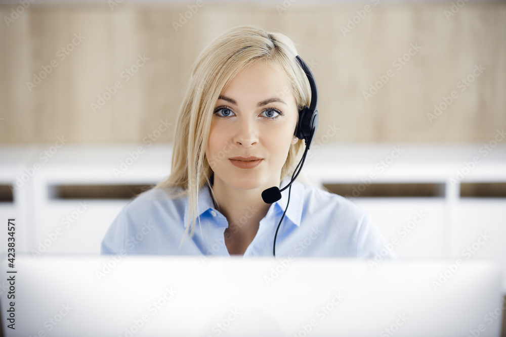 Blonde business woman sitting and communicated by headset in call center office. Concept of telesales business or home office occupation Blonde business woman sitting and communicated by headset in call center office. Concept of telesales business or home office occupation