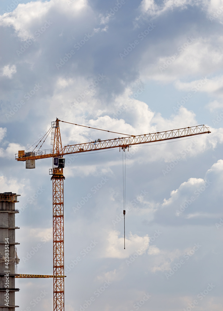 Yellow construction tower crane on the background of clouds