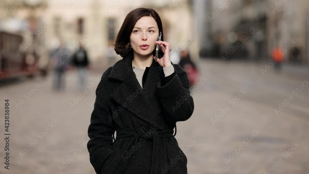 Angry brunette woman yelling at a cell phone in the city street. Negative emotions. Facial expression. Upset girl talking on a smartphone