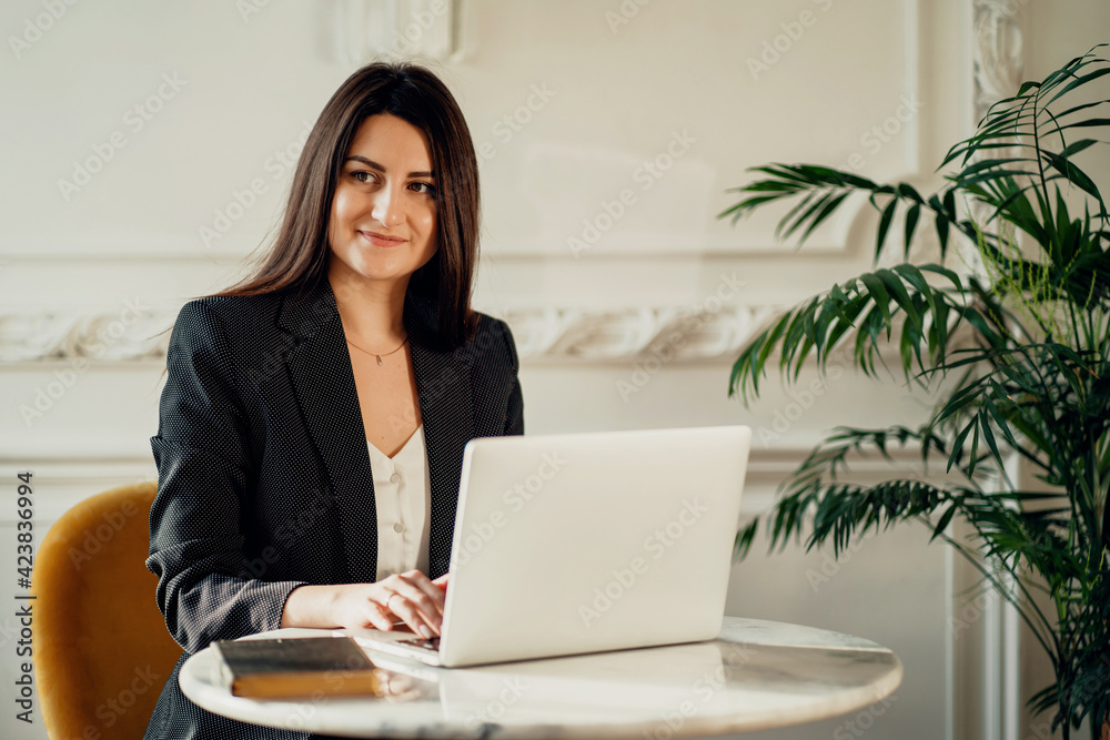 The lawyer is a brunette woman of European appearance. A confident financial manager. Works prints on a laptop computer. Located in a modern office workplace coworking.