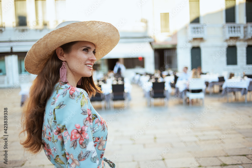 happy stylish woman in floral dress with hat sightseeing