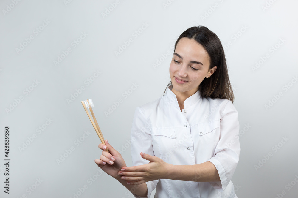 A young brunette girl holds an ecological toothbrush in her hands. A girl in a white coat promotes zero waste. A young brunette girl holds an ecological toothbrush in her hands. A girl in a white coat promotes zero waste.