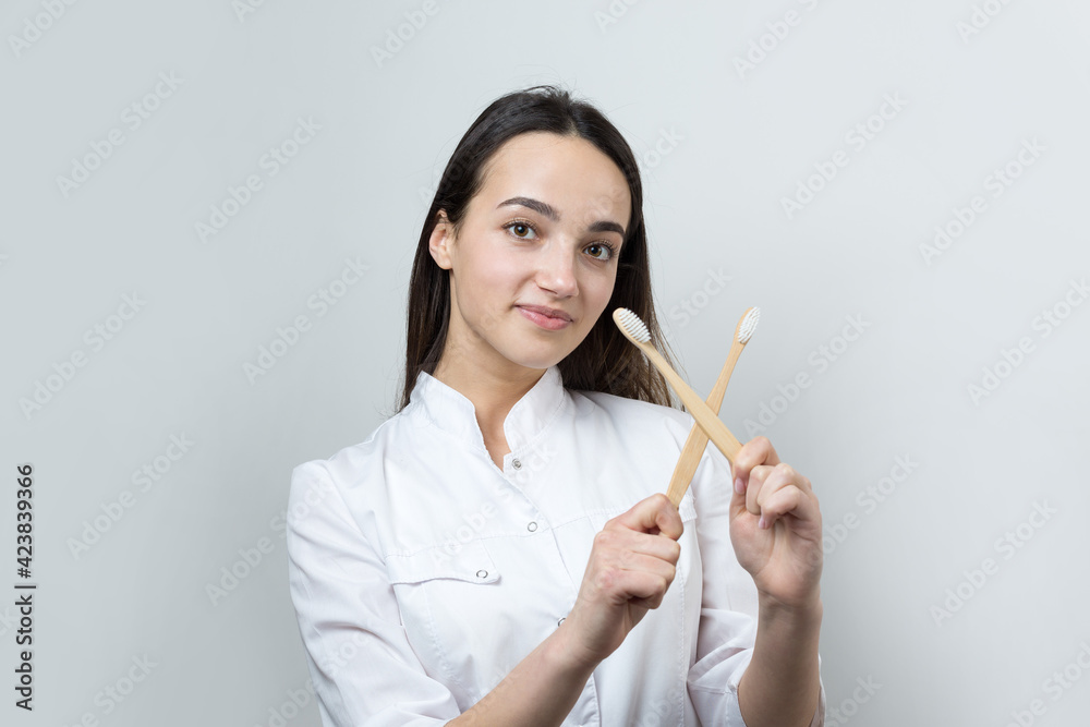 A young brunette girl holds an ecological toothbrush in her hands. A girl in a white coat promotes zero waste. A young brunette girl holds an ecological toothbrush in her hands. A girl in a white coat promotes zero waste.