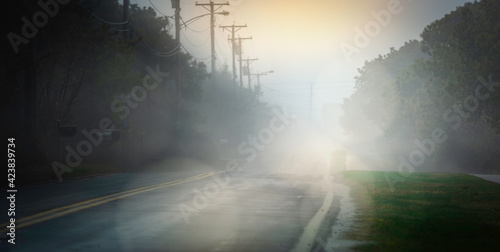 Foggy Road after Rain Storm in Nantucket Island. Rising Sunrays Blinding the Driver's Eyes. Driver's View Point on the Roadside Shoulder. 