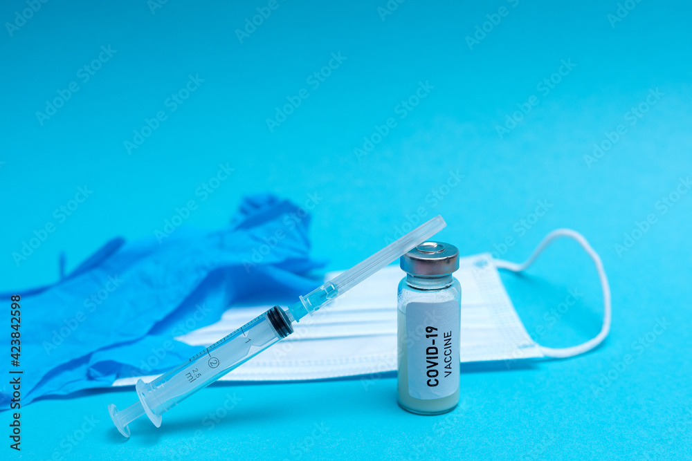 Vaccine on a glass bottle with medicine mask, syringe and blue gloves on blue background