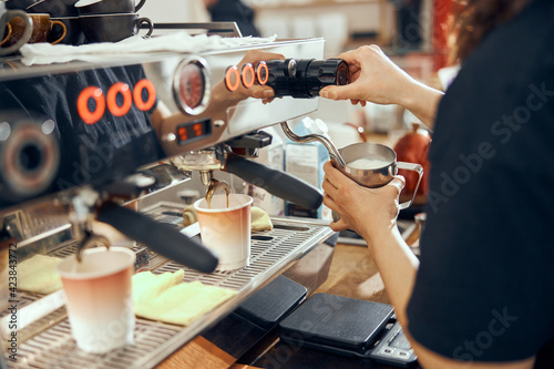 Image of female barista using coffee-making machine to steam milk in cafe