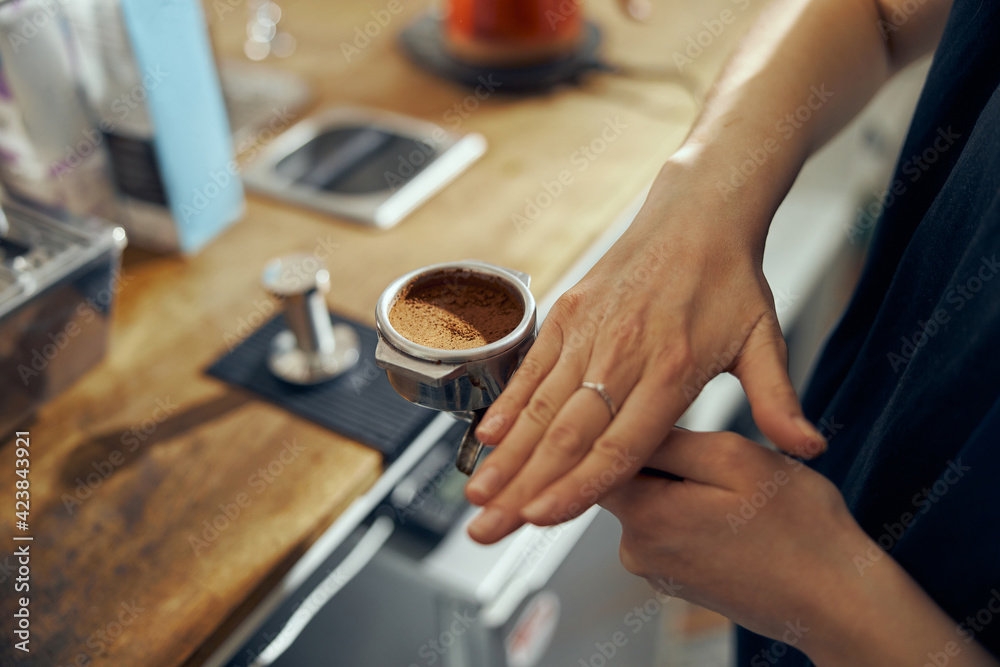 Barista holding coffee holder with ground coffee near professional coffee machine, close up