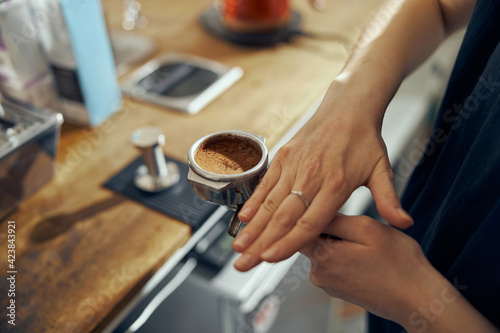 Barista holding coffee holder with ground coffee near professional coffee machine, close up