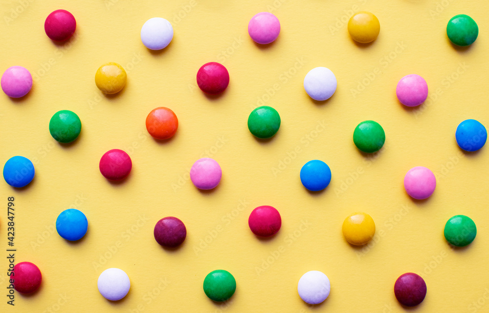 Colored balls of sugar on a yellow background. Chocolate candies covered with multicolored sugar glaze. Colored balls of sugar on a yellow background. Chocolate candies covered with multicolored sugar glaze.