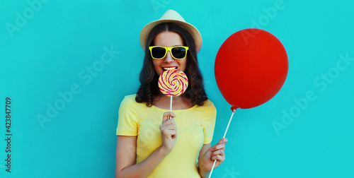 Portrait of happy smiling woman with lollipop and red balloon wearing a summer straw hat on a blue background