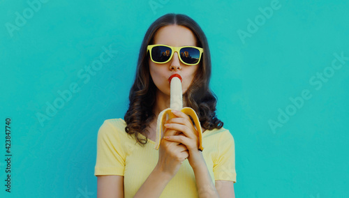 Portrait of young woman eating banana on a blue background