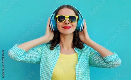 Portrait of happy young woman with wireless headphones listening to music on a blue background