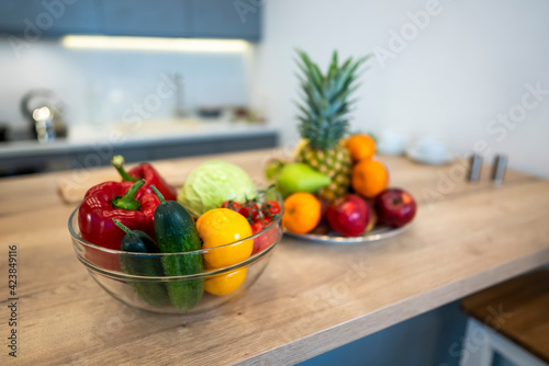 Fototapeta Naklejka Na Ścianę i Meble -  Fruits And Vegetables On The Table Of Modern Kitchen Choice between fruits and vegetables on the table of modern kitchen. Vegan nutrition