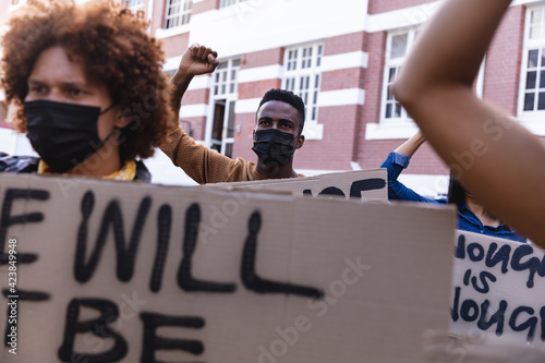 Diverse male and female protesters on march in face masks holding protest signs and raising fists