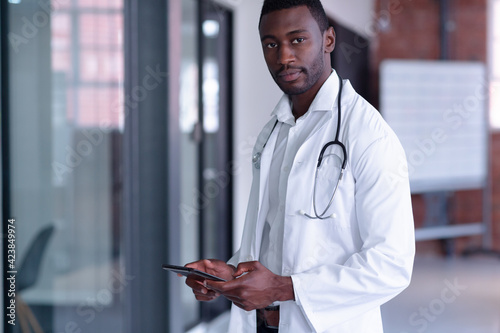 Portrait of african american male doctor wearing white coat and stethoscope using digital tablet