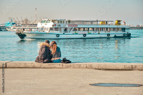 Turkey istanbul 04.03.2021. Two young couples and lovers hugging each other and sitting against bosporus in Kadikoy istanbul during sunny day with passenger ferry and turquoise water background.