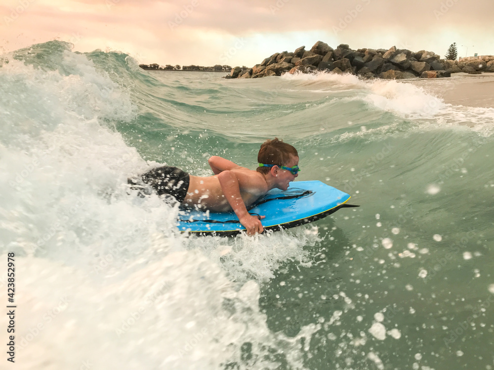 Foto Stock Young boy surfing boogie board on beach wave with groin in