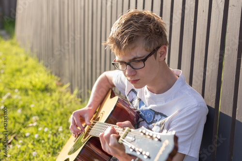 Young teen boy playing acoustic guitar by fence photo