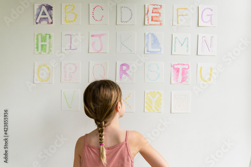 Rear view of girl (8-9) looking at alphabet on wall
