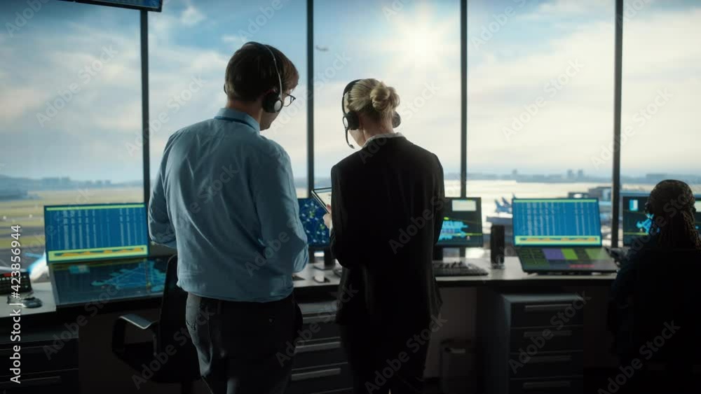 Female and Male Air Traffic Controllers with Headsets Talk in Airport Tower. Office Room is Full of Desktop Computer Displays with Navigation Screens, Airplane Flight Radar Data for the Team. Female and Male Air Traffic Controllers with Headsets Talk in Airport Tower. Office Room is Full of Desktop Computer Displays with Navigation Screens, Airplane Flight Radar Data for the Team.