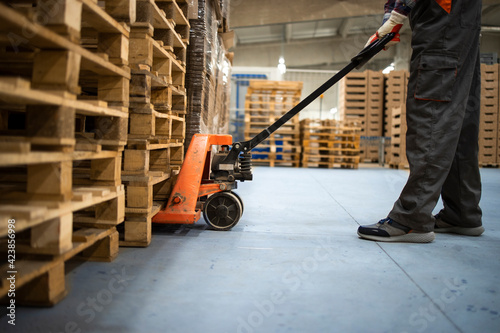 Working at warehouse. Low angle view of unrecognizable worker lifting palette with manual forklift. photo