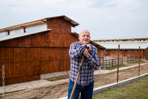 Portrait of successful farmer with pitchfork tool. In background wooden farmhouse. © littlewolf1989