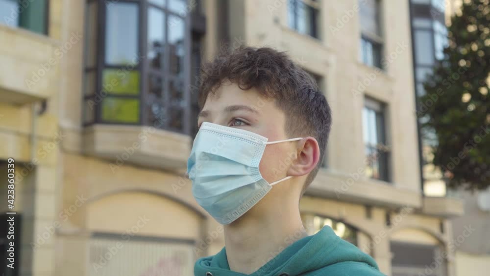A young man puts on and adjusts a medical mask on his face for ease of use on an old European city street with ancient buildings in blur. Travel concept A young man puts on and adjusts a medical mask on his face for ease of use on an old European city street with ancient buildings in blur. Travel concept