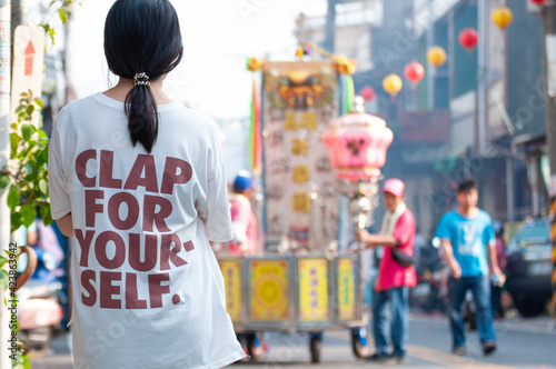 Girl wearing a T-shirt with word, CLAP FOR YOURSELF, is watching traditional temple fair. 