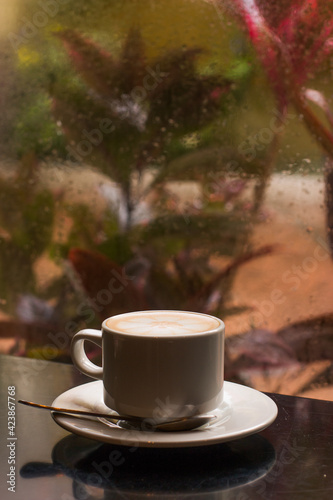 Closeup of a cup of coffee on a window with raindrops in winter weather