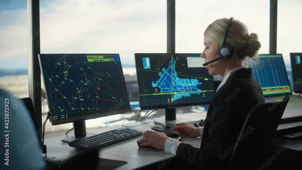 Female Air Traffic Controller with Headset Talk on a Call in Airport Tower. Office Room is Full of Desktop Computer Displays with Navigation Screens, Airplane Departure and Arrival Data for the Team. Female Air Traffic Controller with Headset Talk on a Call in Airport Tower. Office Room is Full of Desktop Computer Displays with Navigation Screens, Airplane Departure and Arrival Data for the Team.
