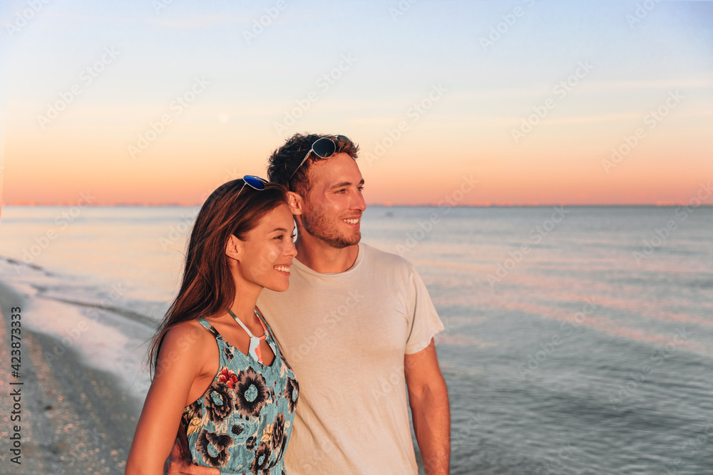 Interracial couple walking on Florida beach watching sunset. Young happy Asian woman and Caucasian man smiling natural beauty outdoor portrait. USA travel vacation.