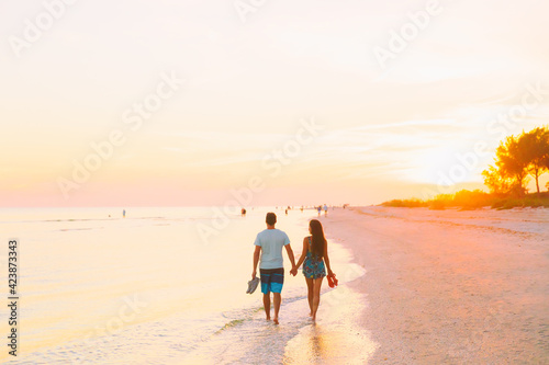Couple walking on beach during romantic sunset on Florida holiday. Silhouette of young man and woman holding hands happy to be on vacation.