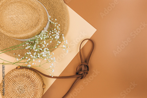 Tropical straw hat, bag, summer flowers on beige brown background. Trendy tropical pattern. Fashion clothing and accessories. Flat lay, close up. Summer, vacation, holidays concept.