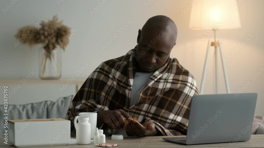 Sick Black Man Taking Pills Sitting Wrapped In Blanket Indoors Sick Black Man Taking Pills Sitting Wrapped In Blanket Indoors