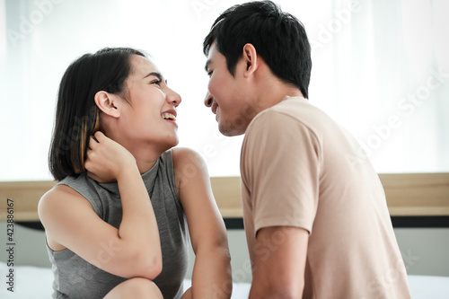 Cute smiling young Asian lover couple lying on the bed, looking at each other while talking funny in the bedroom at home. Concept of happy boyfriend and girlfriend living together
