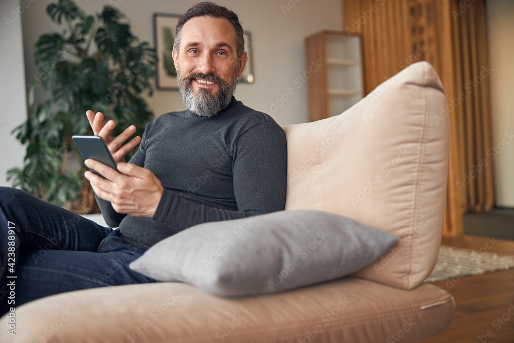 Fototapeta premium Caucasian adult man is sitting with smartpone in modern cozy office lounge zone
