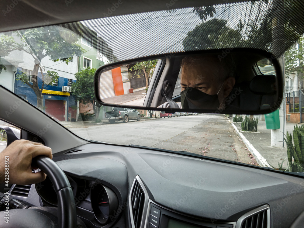 Driver of a car with mask for protection from Corona Virus (Covid-19) seen through the car's rear view mirror, in Sao Paulo, Brazil.