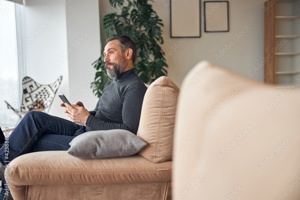 Caucasian adult man is sitting with smartpone in modern cozy office lounge zone Caucasian adult man is sitting with smartpone in modern cozy office lounge zone