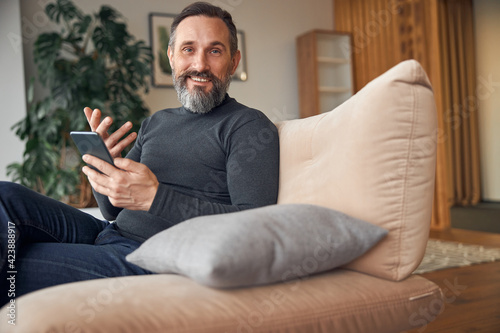 Caucasian adult man is sitting with smartpone in modern cozy office lounge zone