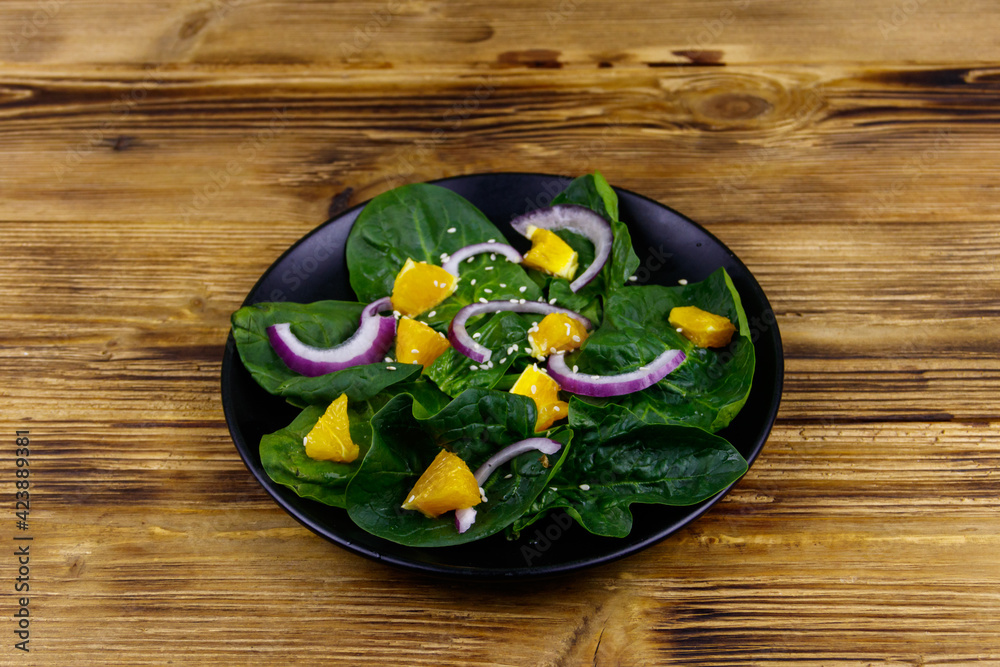 Tasty salad with spinach, orange, red onion and sesame seeds on wooden table. Healthy food or vegetarian concept