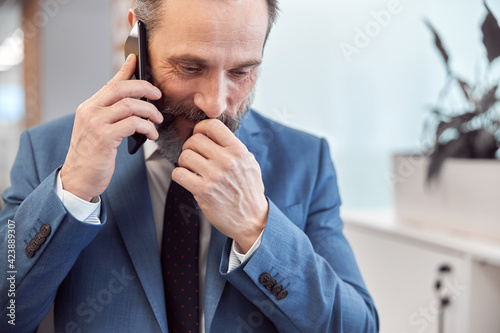 Happy adult caucasian businessman using smarthopne in a modern stylish office