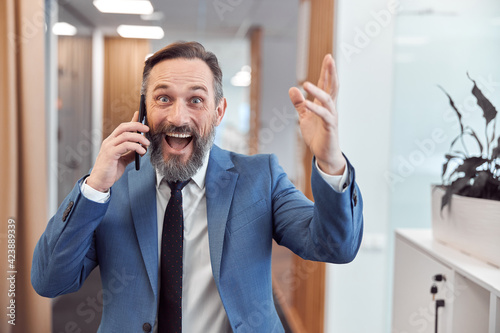 Happy adult caucasian businessman using smarthopne in a modern stylish office