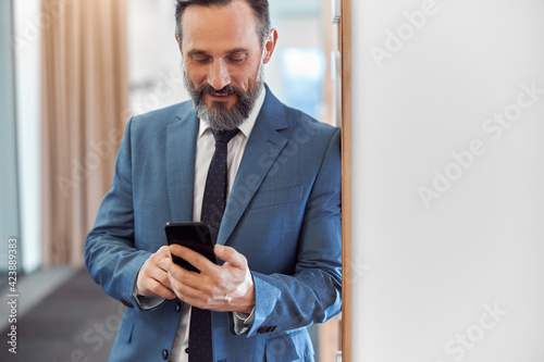 Happy adult caucasian businessman using smarthopne in a modern stylish office
