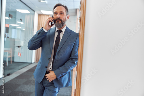 Happy adult caucasian businessman using smarthopne in a modern stylish office