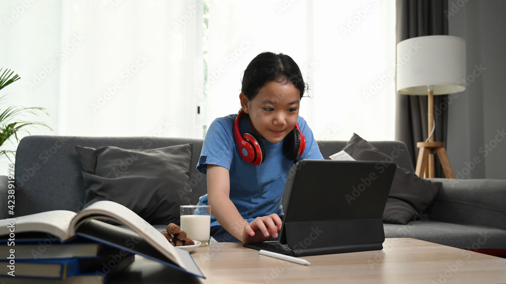 Little girl wearing headphones sitting on sofa and using computer tablet. Little girl wearing headphones sitting on sofa and using computer tablet.