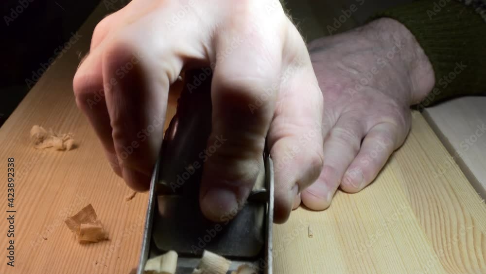 Workshop, woodworking. The master makes a chamfer on the board with a small planer. Close-up. Workshop, woodworking. The master makes a chamfer on the board with a small planer. Close-up.