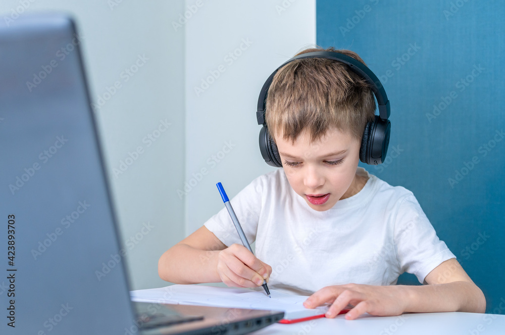 Llittle boy with headphones performs an online lesson. Online education. Llittle boy with headphones performs an online lesson. Online education.