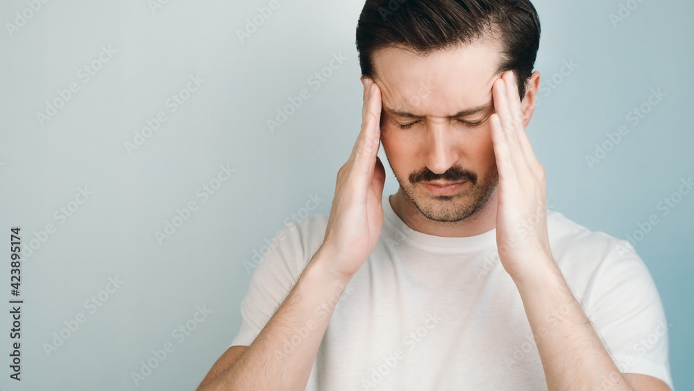 Headache, fatigue concept. Man in white T-shirt is holding his head with hands indoors, massaging the temples. Headache, fatigue concept. Man in white T-shirt is holding his head with hands indoors, massaging the temples.