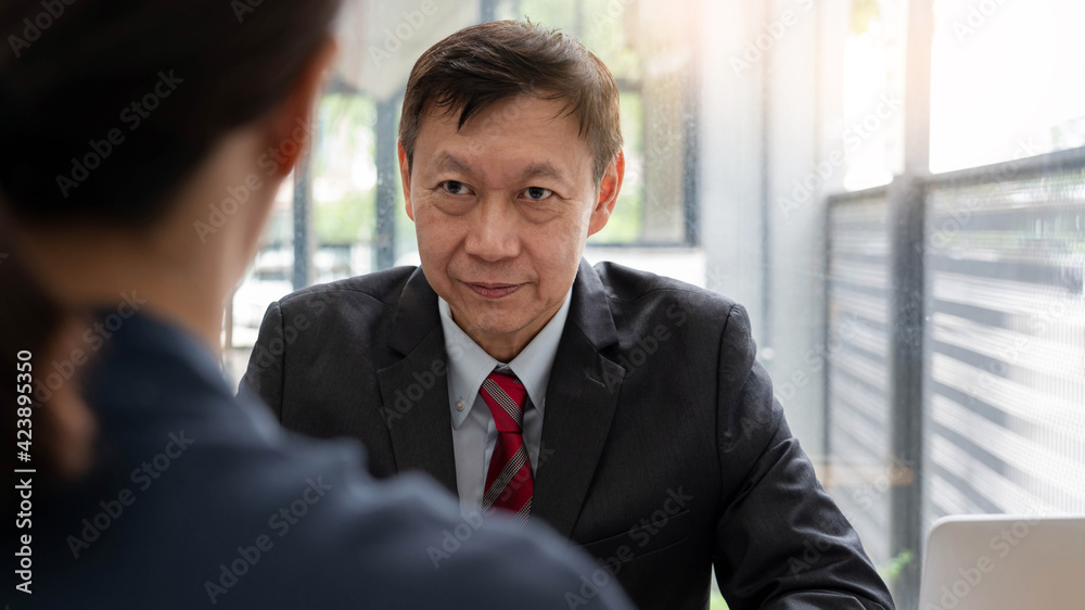 Mature boss senior Asian businessman leadership working together colleagues discuss information over a report document in a meeting in office. Mature boss senior Asian businessman leadership working together colleagues discuss information over a report document in a meeting in office.